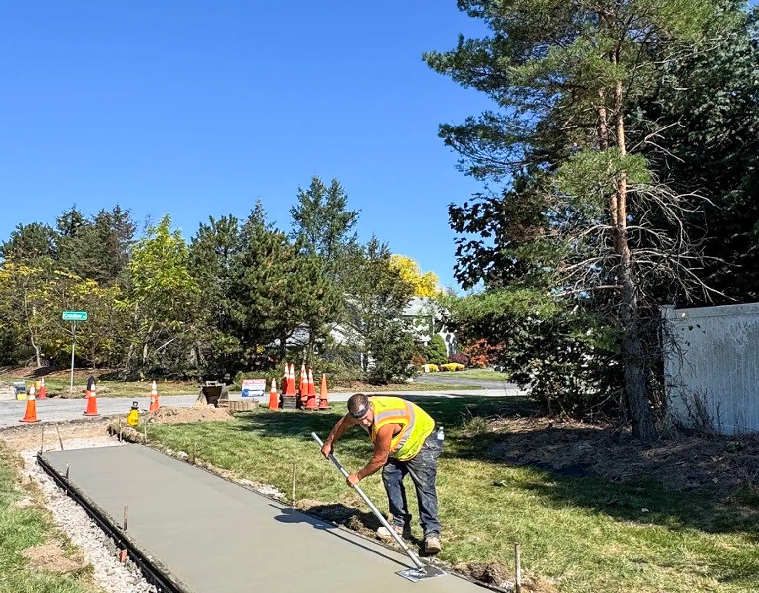 Worker smoothing freshly poured concrete sidewalk along Five Mile Line Road in Penfield
