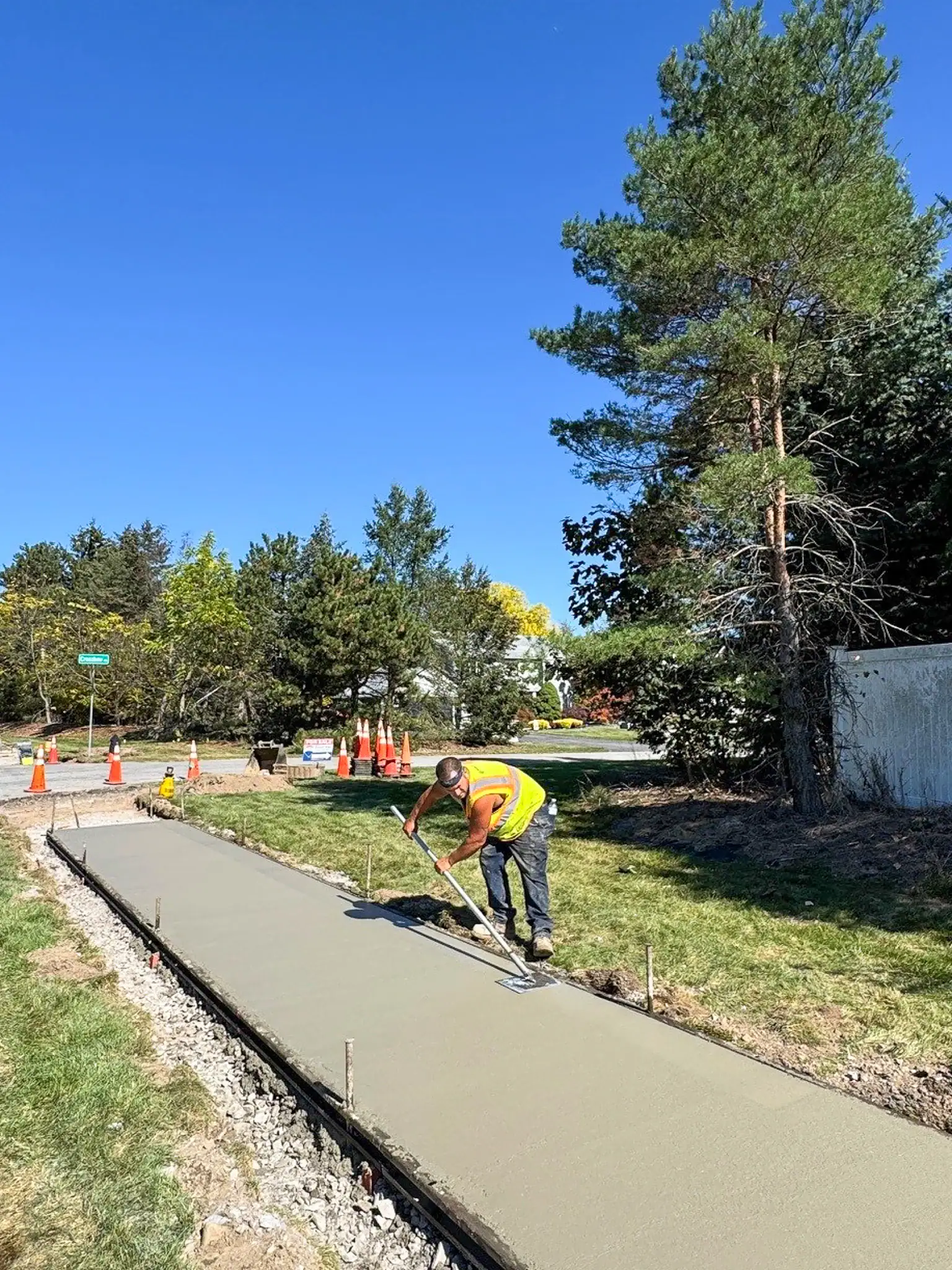 Worker smoothing freshly poured concrete sidewalk along Five Mile Line Road in Penfield
