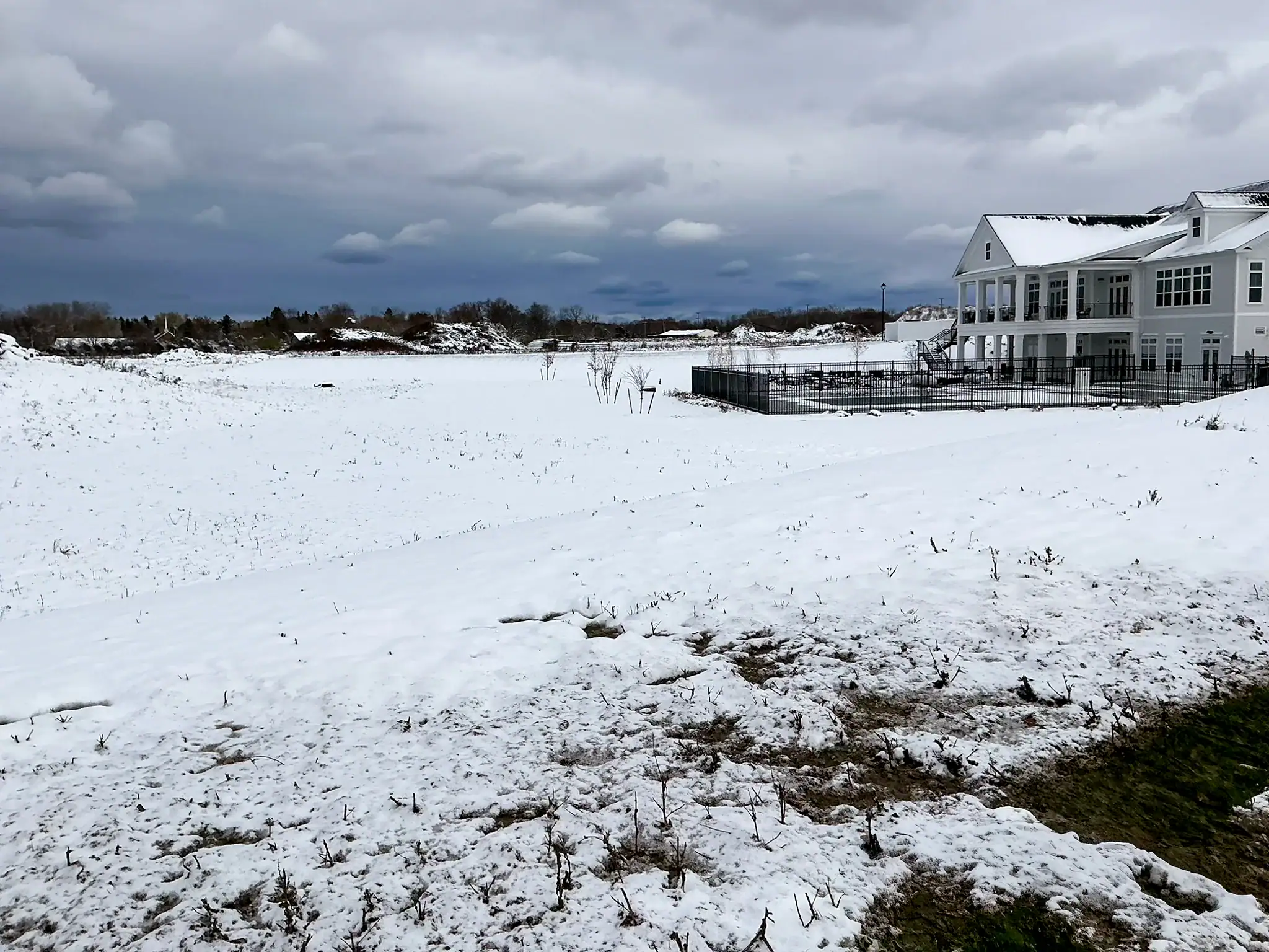 Snow-covered residential construction site at Arbors at Penfield with completed clubhouse building and visible erosion patterns in foreground