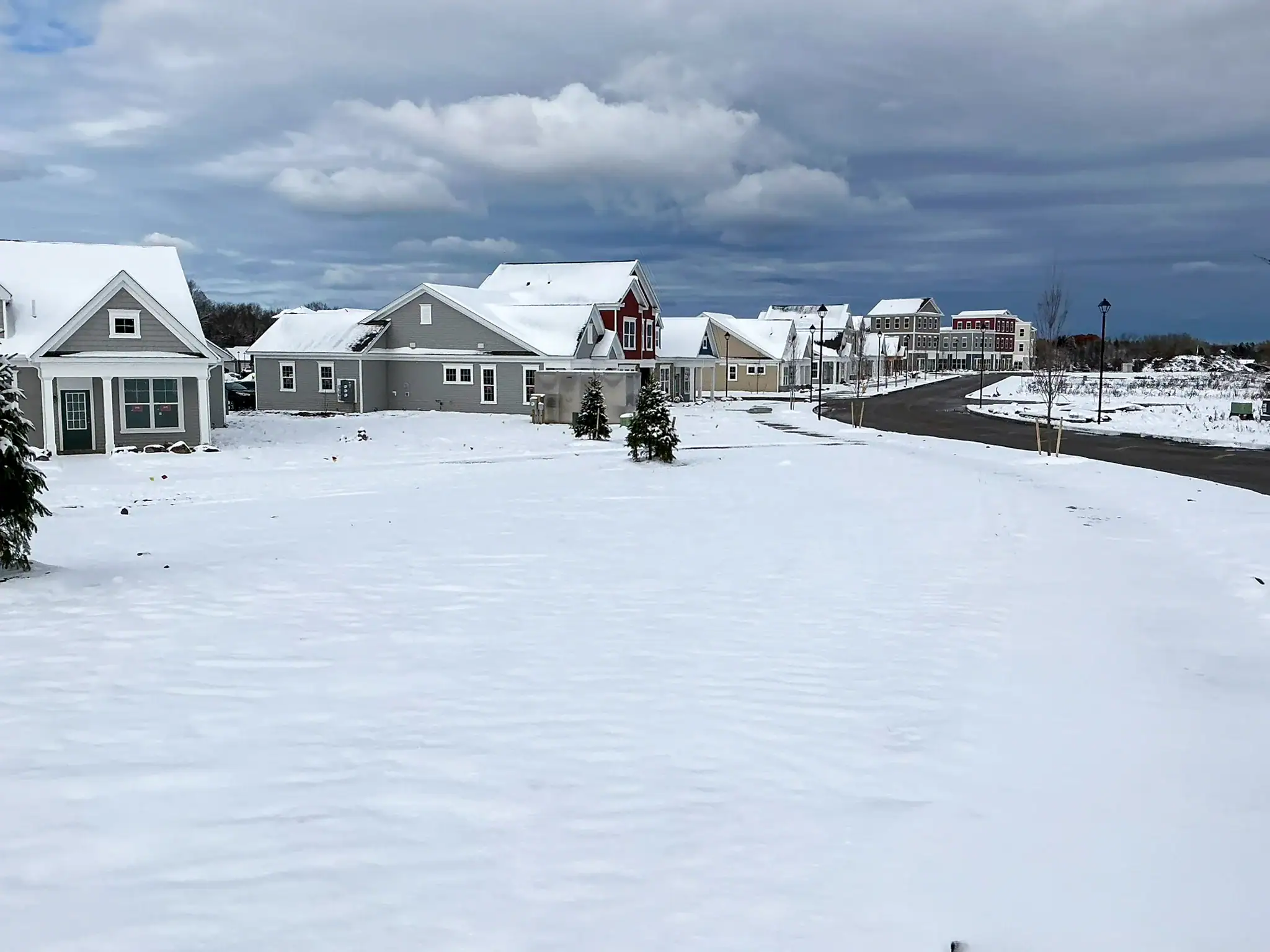 Snow-covered residential street at Arbors at Penfield showing completed homes, landscaping, and clubhouse under winter conditions with dramatic sky