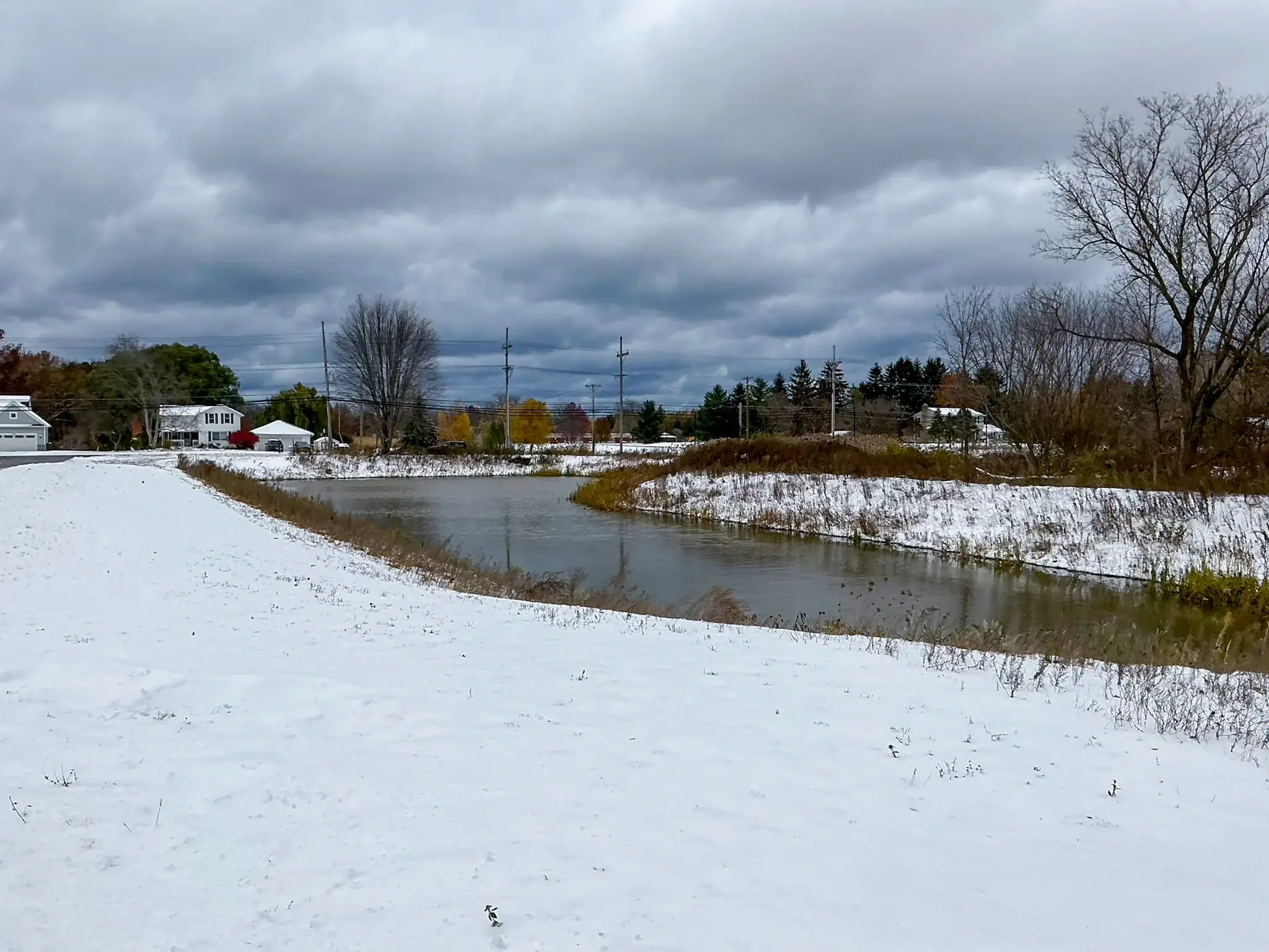 Stormwater detention pond at Bella Terra Place housing development in Rochester NY during winter with snow coverage and vegetated side slopes