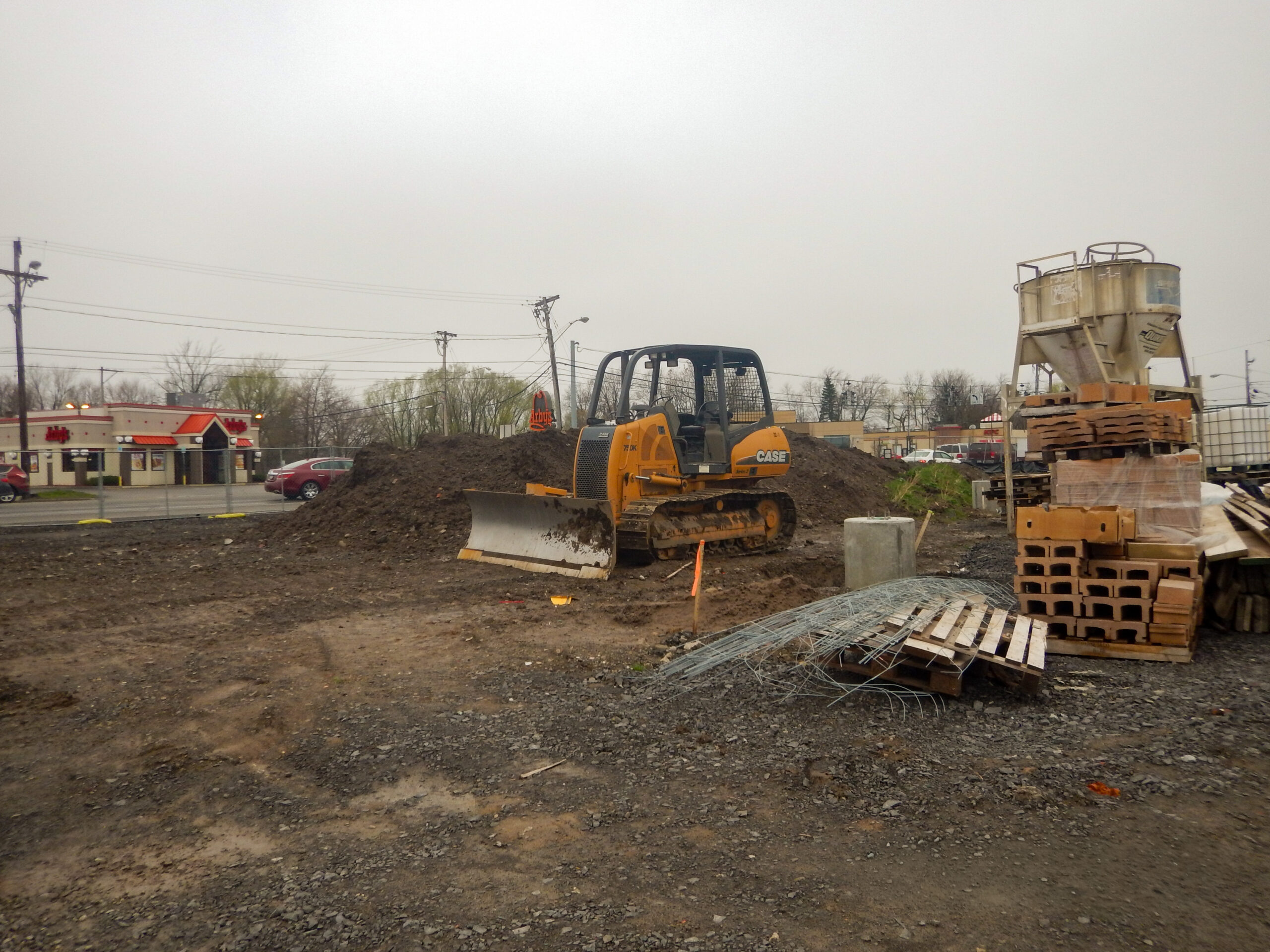 Delta Sonic West Henrietta early site preparation showing CASE bulldozer grading work, earth material piles, staged construction materials, and neighboring commercial properties.