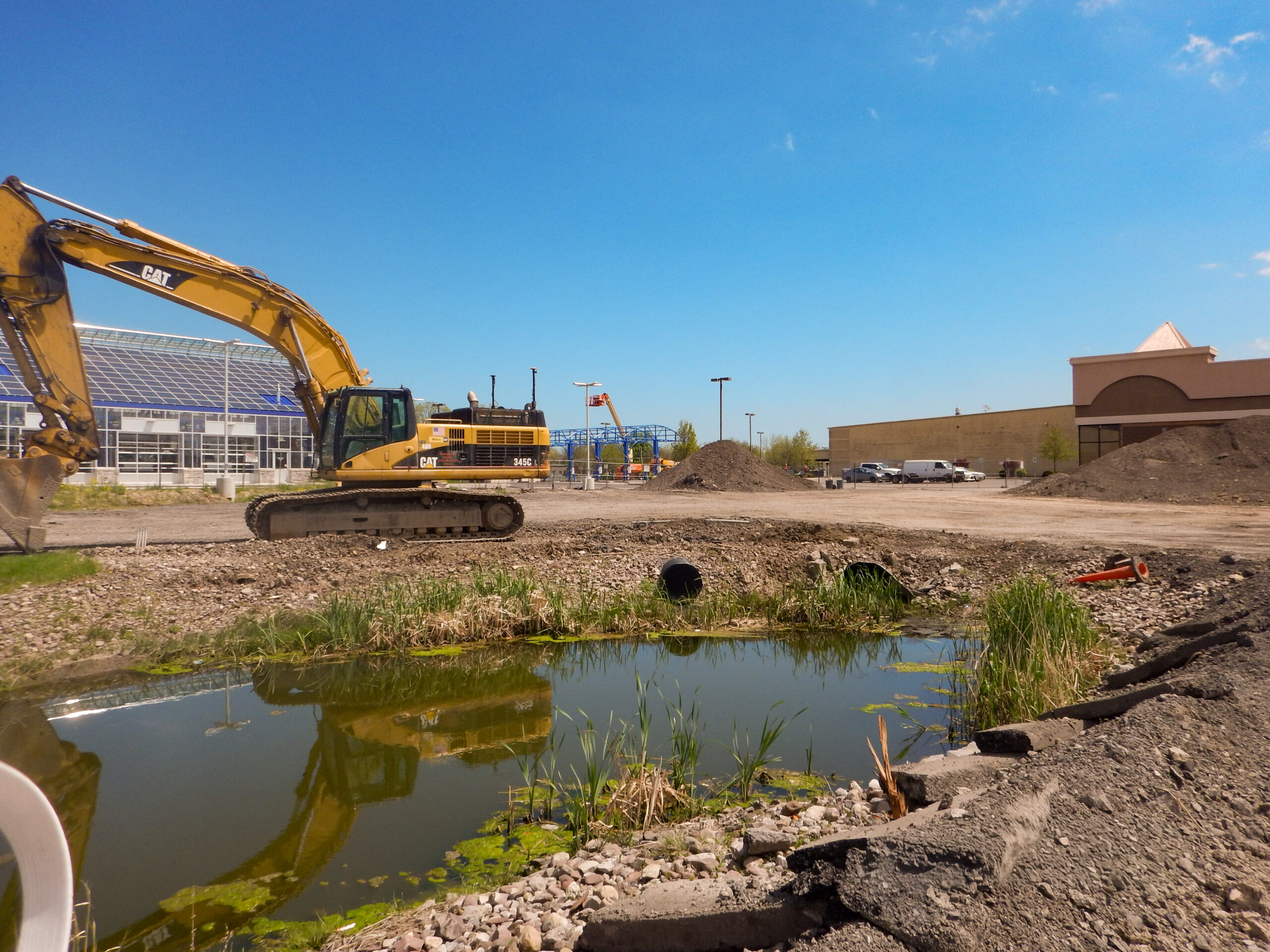 Delta Sonic West Henrietta heavy excavation and grading work showing CAT excavator, raw earthwork, detention pond area, and construction staging during early site preparation.