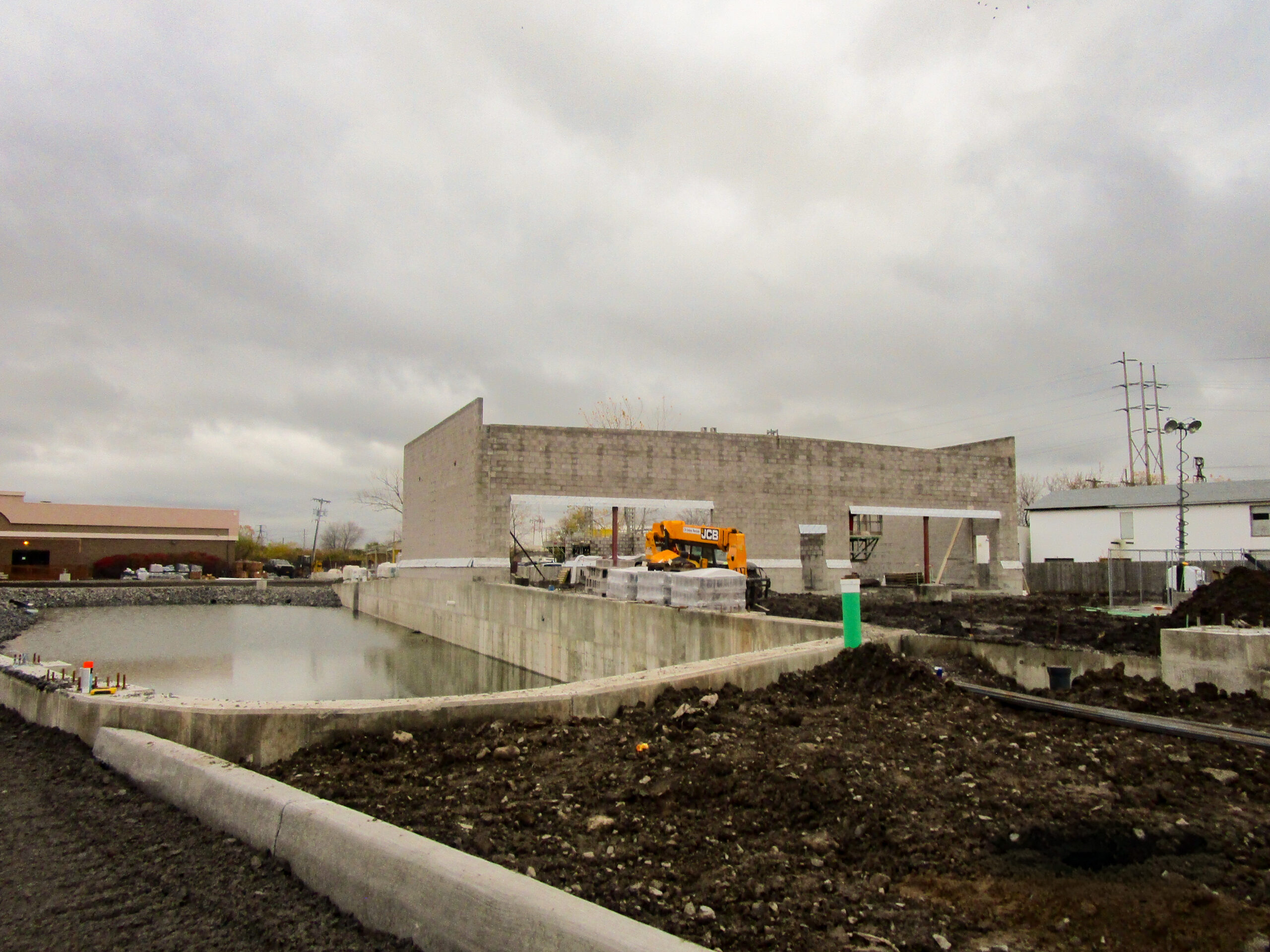 Delta Sonic West Henrietta stormwater detention pond under early construction showing concrete walls, earthwork, and construction equipment during initial site development.