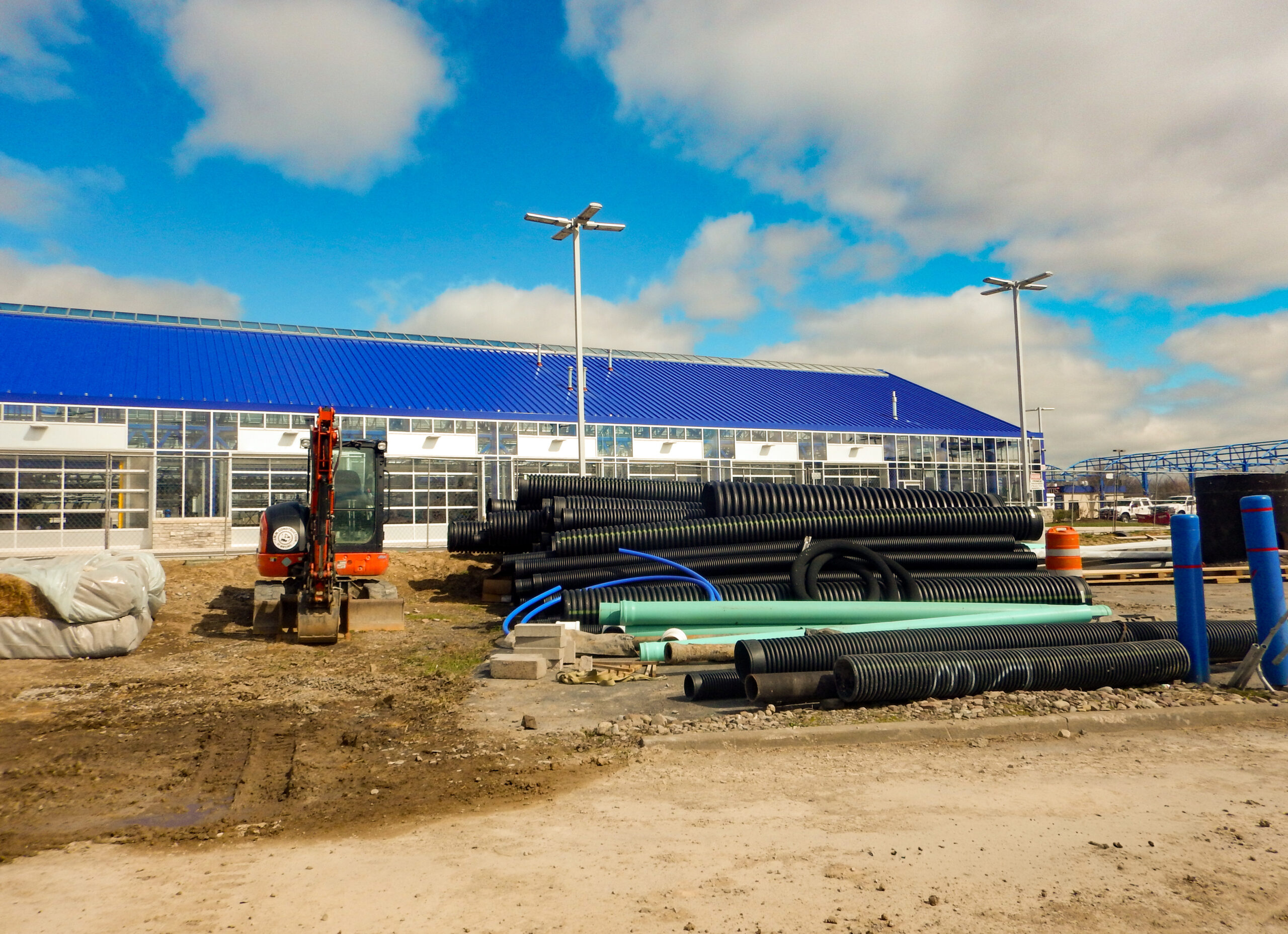 Delta Sonic West Henrietta construction materials staging showing corrugated drainage pipes, utility tubing, and construction equipment near the carwash building during site preparation.