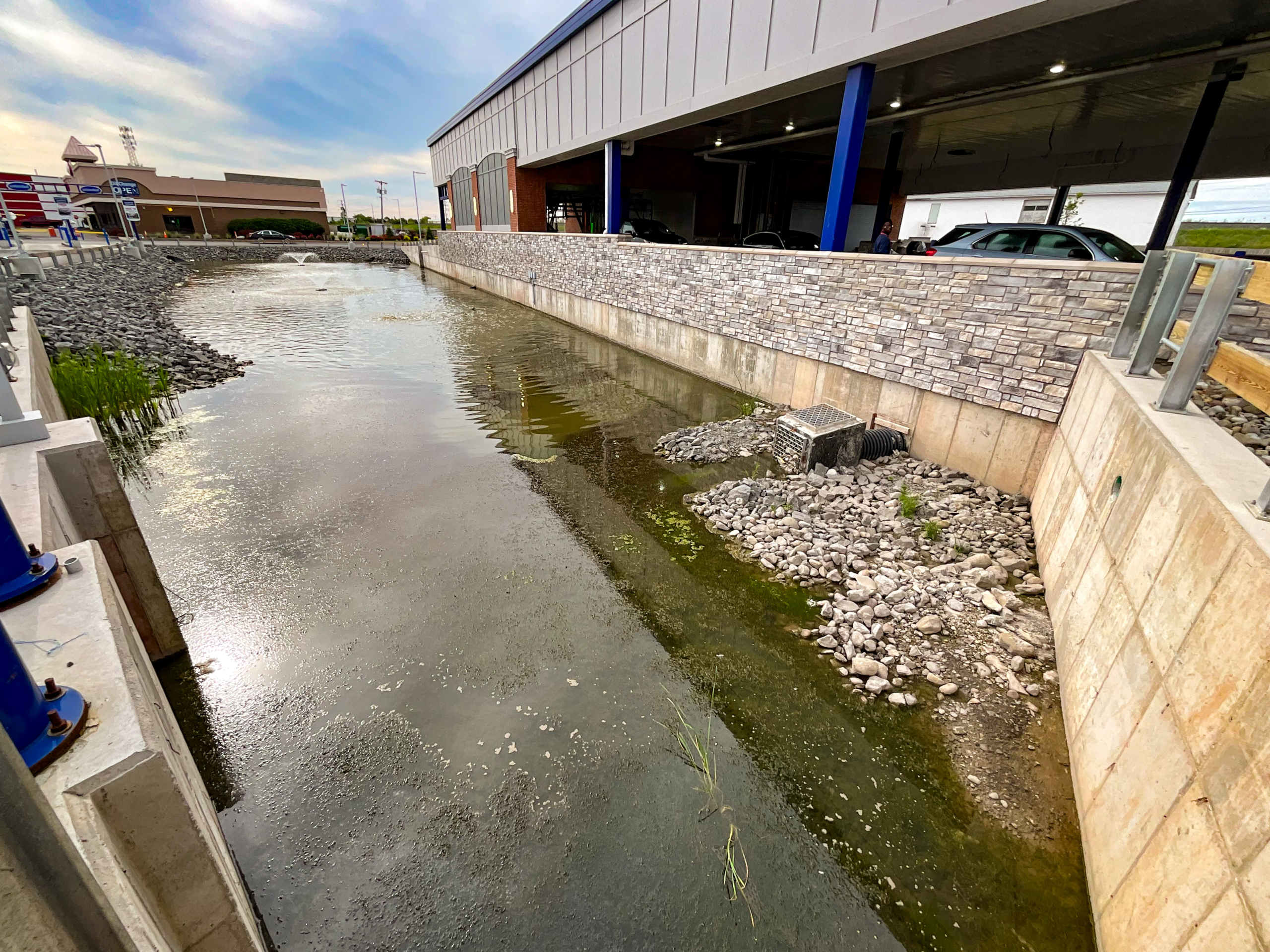Delta Sonic West Henrietta stormwater detention pond showing concrete walls, riprap erosion protection, stone veneer facing, and outlet structure during construction phase.