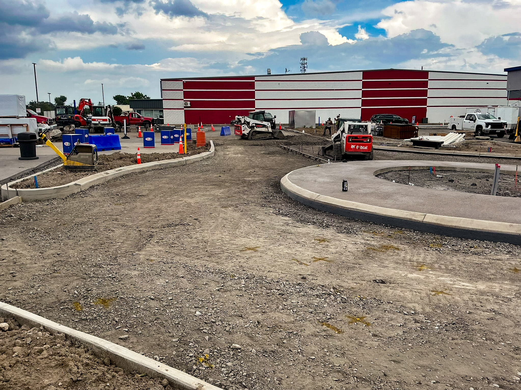 Delta Sonic West Henrietta construction phase showing site grading work, concrete roundabout edging, and earthwork with construction equipment on site.
